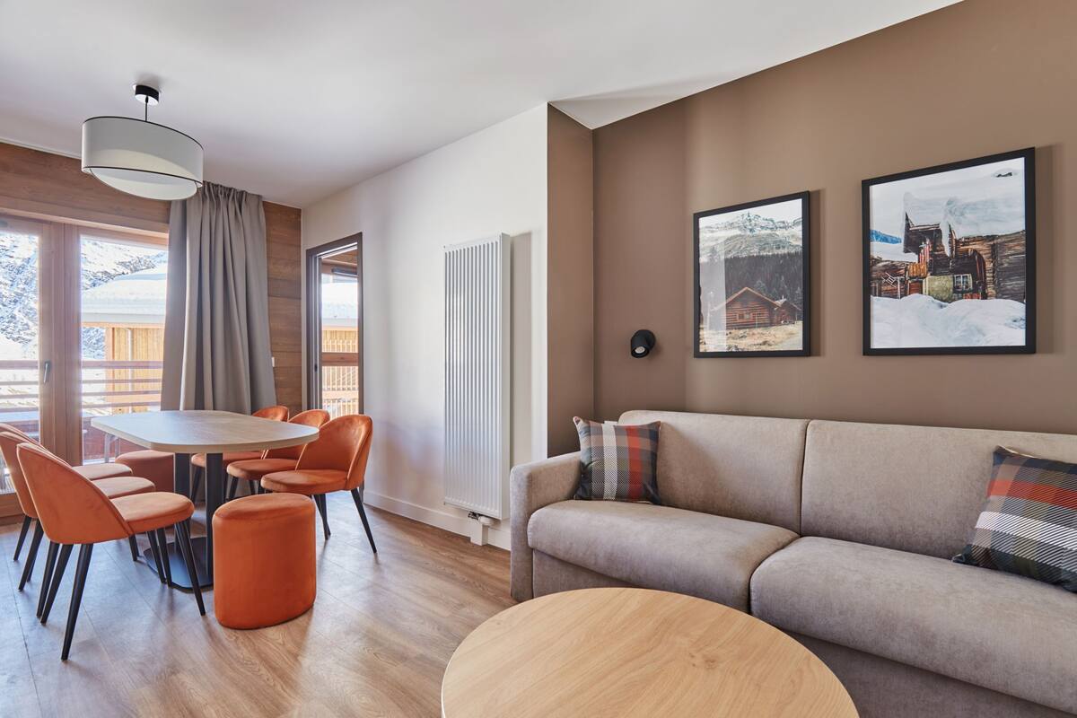 Ein modernes Wohnzimmer mit einer Couch, einem Esstisch mit Stühlen und einem großen Fenster mit Vorhängen.