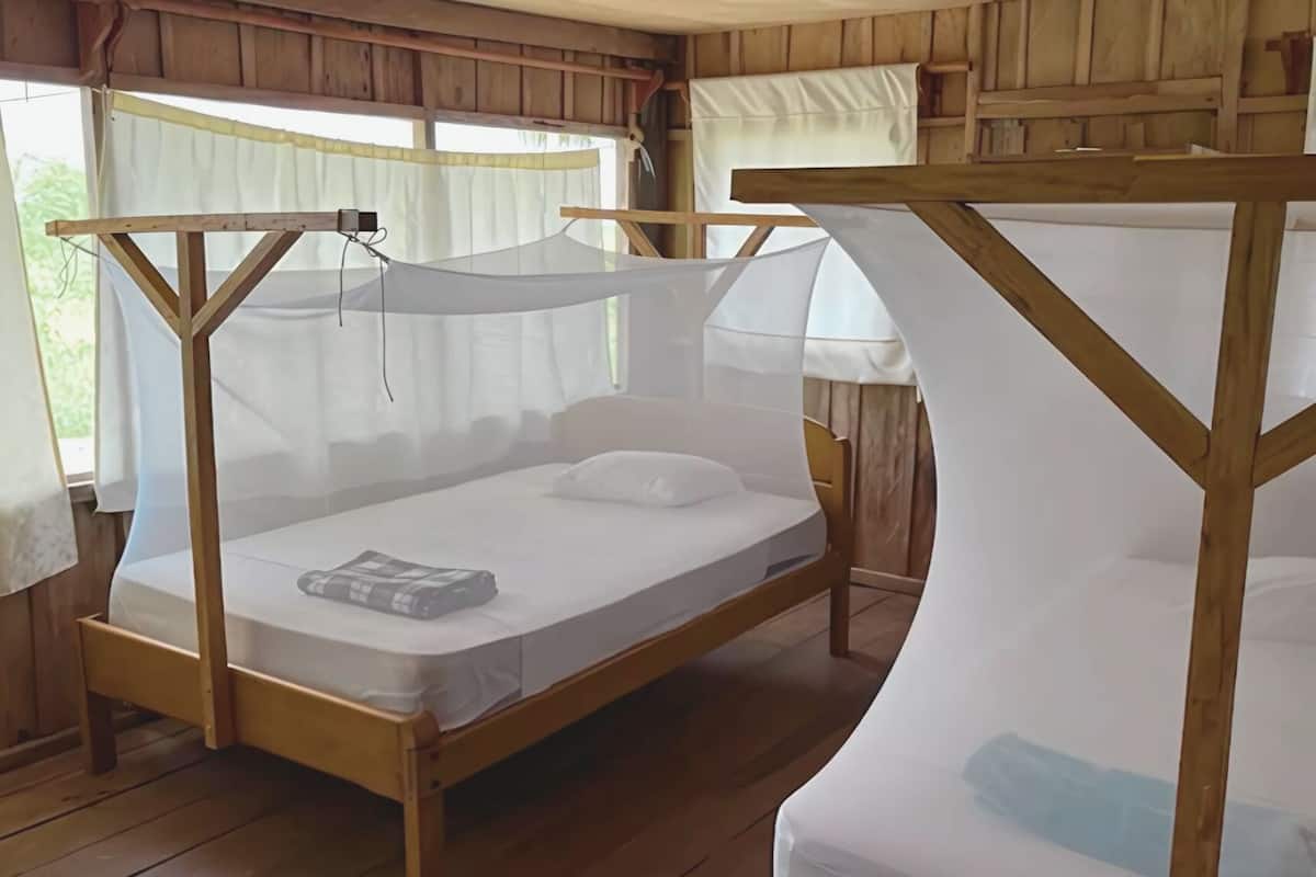 A wooden bed with a mosquito net and a mattress on the floor.