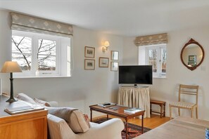 Relax in a cozy seating area with a sofa, chair, and TV on a stand, surrounded by framed pictures and a mirror.