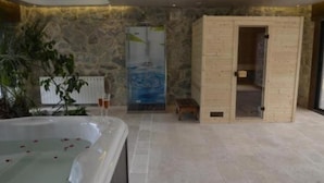 Een wellnessruimte met een ruime jacuzzi, een houten sauna en een achtergrond van een stenen muur.