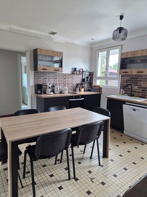 A modern kitchen with a dining area, featuring a brick backsplash, black cabinets, and a wooden dining table with chairs.