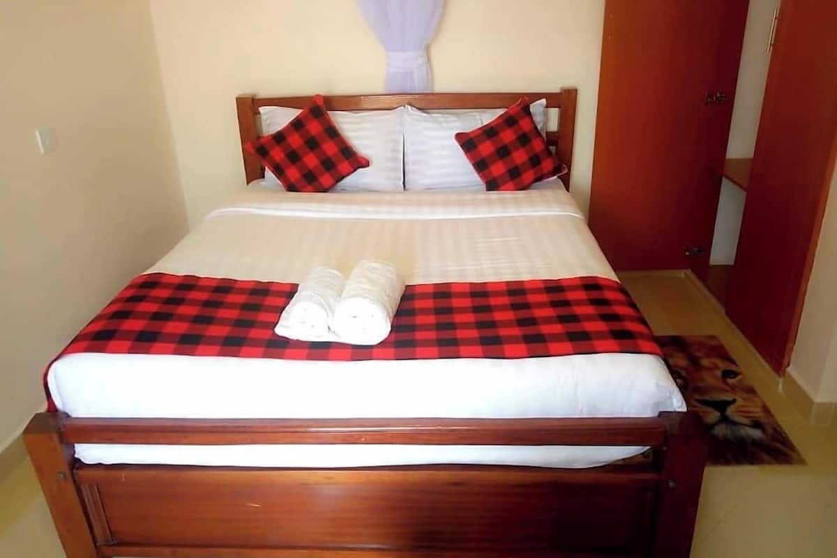 A neatly made bed with a checkered bedspread, two rolled towels, and matching pillows.