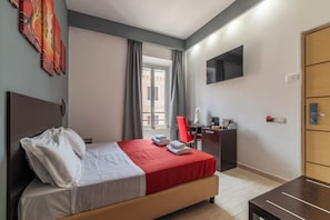 A hotel room with a bed, a desk, a chair, a TV, and a wardrobe.
