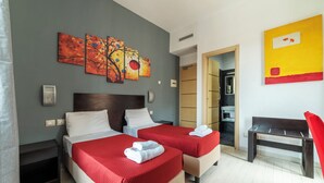 A hotel room with two beds, a bench, and artwork on the walls.