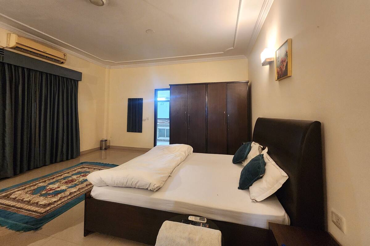 Une chambre d’hôtel avec un lit, une armoire, une table de chevet, une lampe et une vue sur l’extérieur.