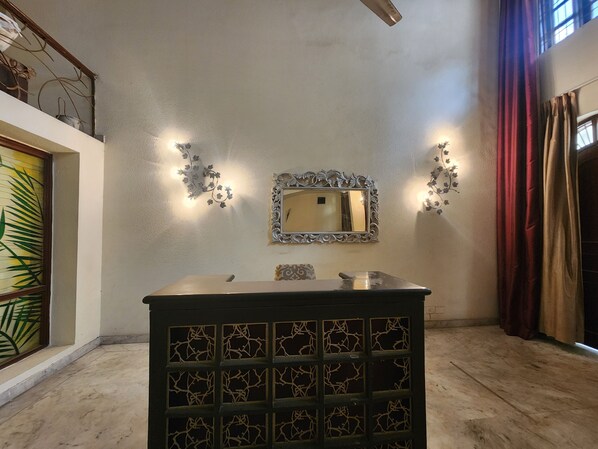Une pièce avec un miroir, des appliques murales décoratives, un meuble orné de motifs et une fenêtre avec des rideaux.