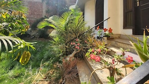 A courtyard with a brick wall, potted plants, and a staircase leading to a balcony. - Hotel The Own Stay-Urban Boutique (New Delhi)