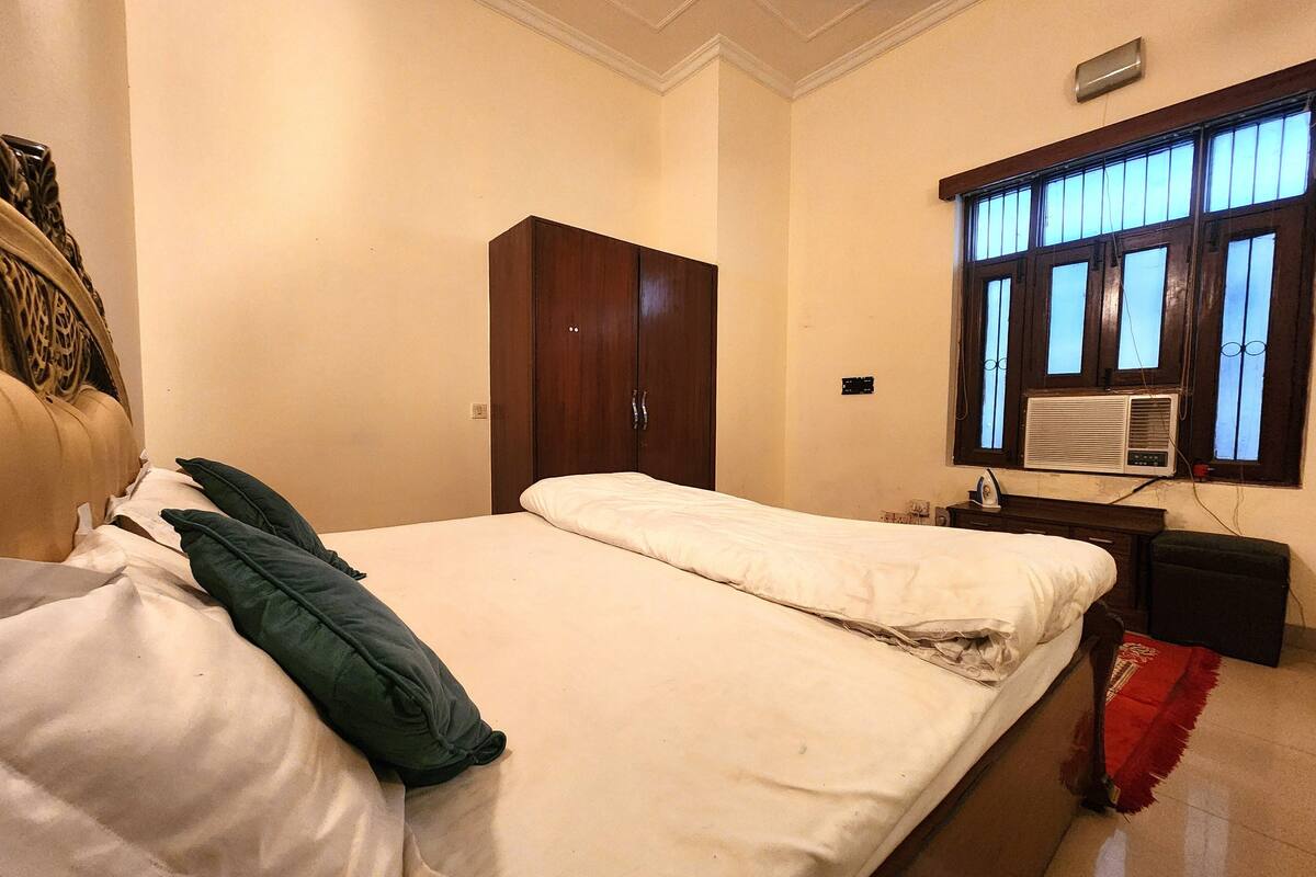 Une chambre à coucher comprenant un lit, une armoire, une fenêtre avec un climatiseur et une prise électrique murale.
