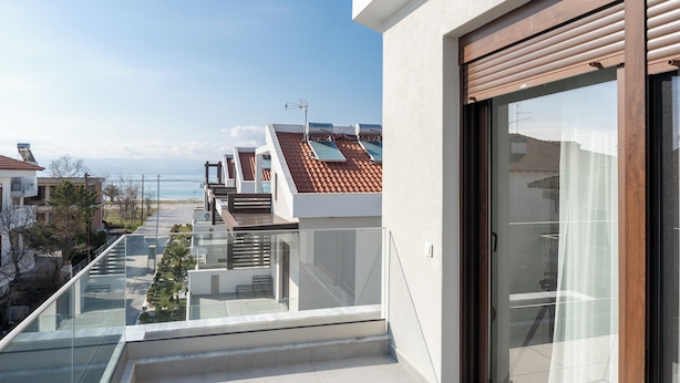 Un immeuble résidentiel moderne doté d’un balcon en verre, offrant une vue sur la mer, et d’un panneau solaire sur le toit.