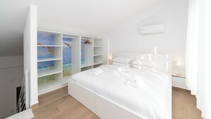 Une chambre moderne avec un grand lit, une armoire intégrée et une vue sur la mer, visible à travers les portes de l’armoire.