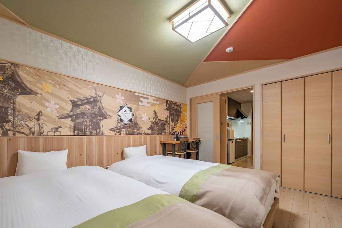 Ein Hotelzimmer mit zwei Betten, einem Esstisch und einer sichtbaren Küchenzeile durch eine offene Tür.