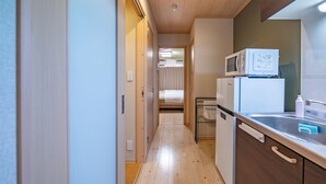A narrow hallway leading to a bedroom with a bed and a kitchenette area with a microwave and a refrigerator. - Stay Maison Hida Takayama (Takayama)