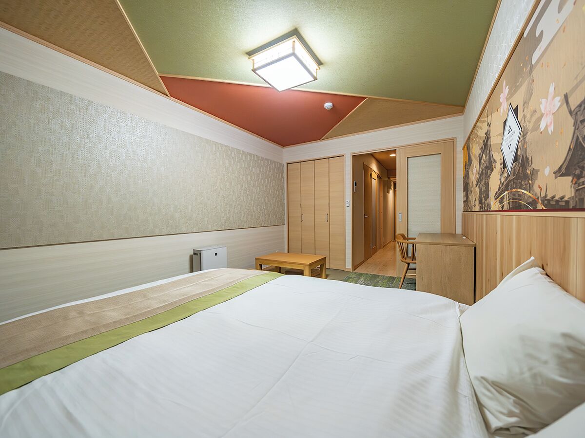 Quarto de hotel com cama, escrivaninha, cadeira e guarda-roupa.