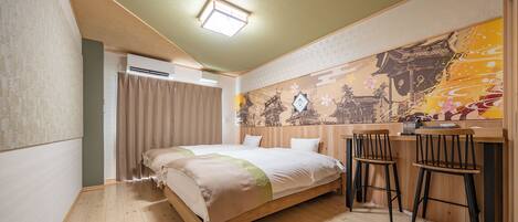 A hotel room with a bed, a desk, two chairs, a window with curtains, and a wall with a mural.