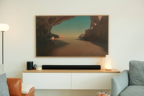 Ein modernes Wohnzimmer mit einem großen Landschaftsbild, einem Flachbildfernseher, einer Lampe und einem Sofa.