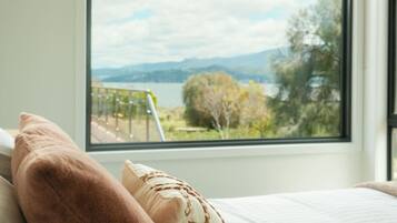 Una camera da letto con un'ampia finestra, un letto e vista su un lago e montagne.