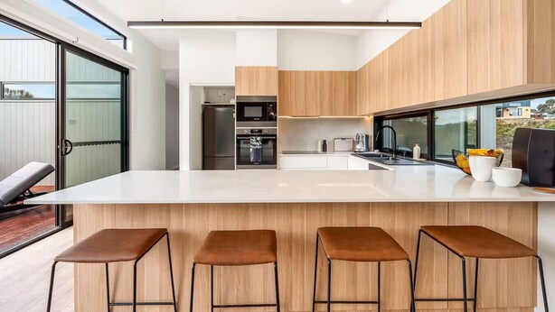 A modern kitchen with a large island, bar stools, and a view of the outdoors. - Waterfront Luxury in Opossum Bay (Opossum Bay)