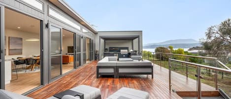 Een modern terras buiten, met een bank en stoelen, een eethoek met tafel en stoelen, en uitzicht op het landschap.