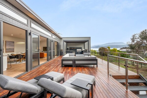 Eine moderne Außenterrasse mit einer Couch und Sesseln, einem Essbereich mit Tisch und Stühlen und Blick auf die Landschaft.