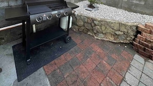 An outdoor grill setup in a backyard with a wooden fence, stone wall, and a small garden. - Renovated two-level Sandy Bay apartment (Sandy Bay)