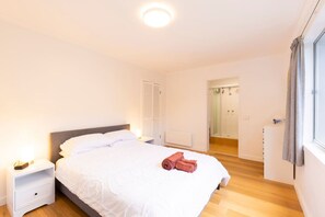 A bedroom with a bed, nightstand, and a bathroom visible through an open door. - Renovated two-level Sandy Bay apartment (Sandy Bay)
