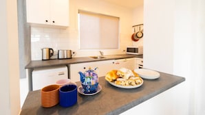 A modern kitchen with white cabinets, a stainless steel kettle, a microwave, and a plate of pastries. - Renovated two-level Sandy Bay apartment (Sandy Bay)