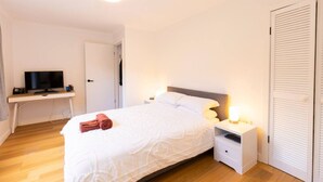 A bedroom with a bed, bedside tables, a desk with a television, and a closet. - Renovated two-level Sandy Bay apartment (Sandy Bay)