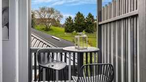 Un balcon avec deux chaises et une lanterne, donnant sur un paysage verdoyant parsemé d’arbres et bordé d’une clôture.
