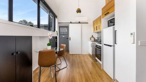 Une cuisine moderne avec un coin repas, dotée d’un plancher en bois, de meubles blancs et d’un luminaire suspendu.