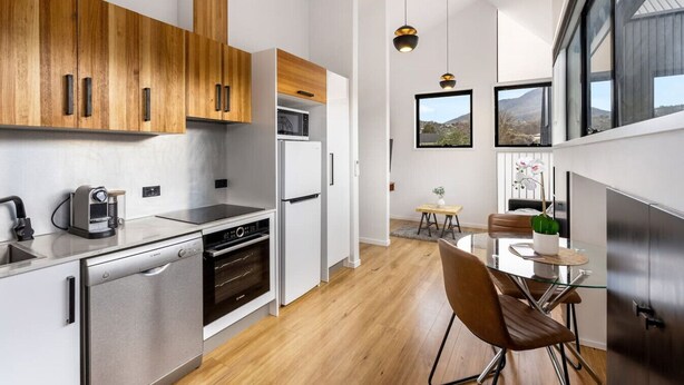 Une cuisine moderne avec des meubles en bois, des appareils électroménagers en acier inoxydable et un coin repas offrant une vue sur les montagnes.