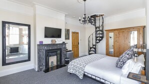 A bedroom with a fireplace, a bed with patterned bedding, a large mirror, and a television. - Apartment in Brighton near Brighton Beach (Brighton)