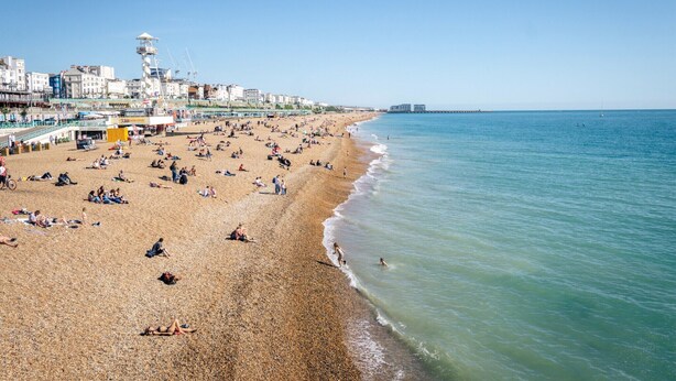 A beach with people sunbathing and swimming, a lifeguard tower, and buildings in the background. - Apartment in Brighton near Brighton Beach (Brighton)