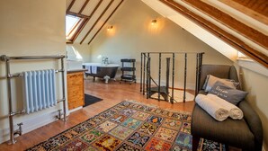 A cozy attic bedroom with a sloped ceiling, a bathtub, a wooden cabinet, a patterned rug, and a comfortable chair with a rolled towel. - Apartment in Brighton near Brighton Beach (Brighton)