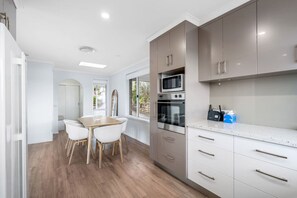 A modern kitchen with white cabinets, a dining table with chairs, and a large window providing a view of the outdoors. - Spectacular View Modern Comfort (Sandy Bay)