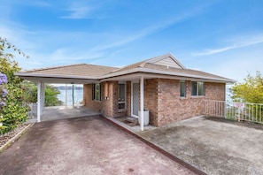 A two-story house with a covered porch, brick exterior, and a view of the water.