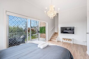 Ein Schlafzimmer mit einem großen Bett, einem an der Wand montierten Fernseher und einem Balkon mit Blick ins Freie.