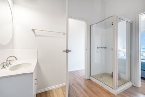 A modern bathroom with a white sink, a glass shower enclosure, and a door leading to a bedroom with a view.