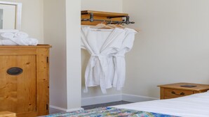 Een hotelkamer met een houten garderobe, een bed met een kleurrijk sprei en een nachtkastje van hout met een boek.