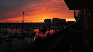 Een jachthaven bij zonsondergang, met aangemeerde boten en gebouwen op de achtergrond.