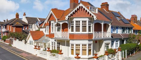 Una casa de estilo victoriano con ventanal saliente, varios chimeneas y cerca de piquetes blancos.