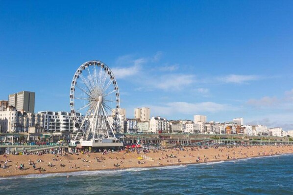 Una playa con una noria y un paisaje urbano al fondo.