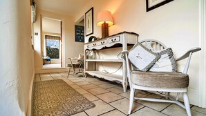 A hallway with a patterned rug, a white chair with a pillow, a lamp, and a shelf with framed pictures. - Holiday Home in Ashbourne near Dovedale Trails (Ashbourne)