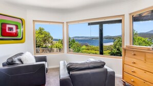 Un salon moderne doté d’une grande fenêtre offrant une vue panoramique sur la mer et les collines.