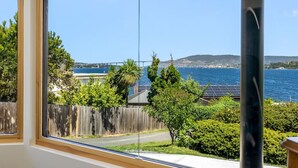 Une pièce dotée de grandes fenêtres donnant sur une zone côtière, une clôture en bois et une vue sur la mer et un pont.