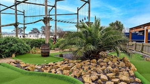 Un campo de mini golf con un jardín de rocas, palmeras y un puente de madera.