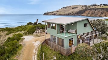 Une maison côtière à deux étages, dotée d’une grande terrasse et offrant une vue sur l’océan.