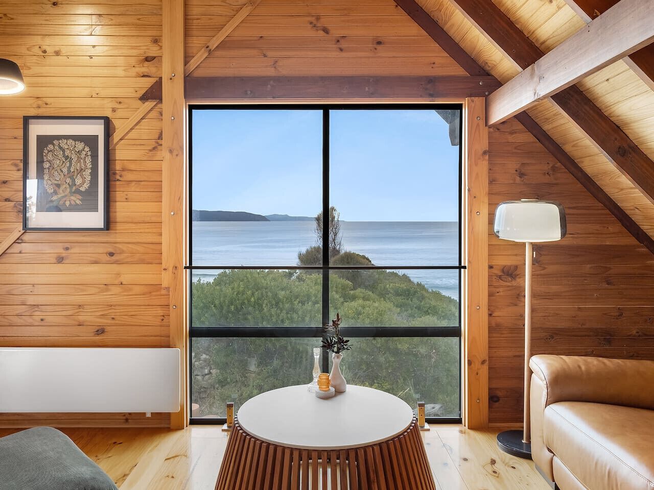 Un interior de madera con un ventanal grande que ofrece vistas al mar y al verdor.