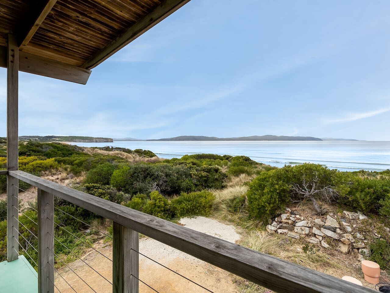 A wooden deck overlooking a coastal landscape with a clear view of the sea and distant hills.
