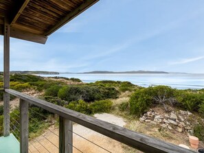 A wooden deck overlooking a coastal landscape with a clear view of the sea and distant hills.