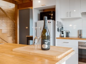 A bottle of wine on a wooden countertop with two glasses.